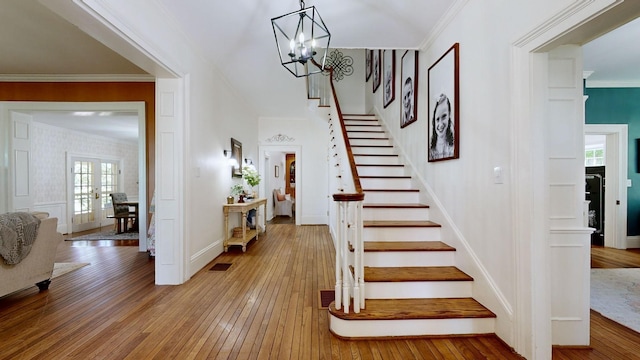 stairs featuring wood-type flooring, a notable chandelier, crown molding, and french doors