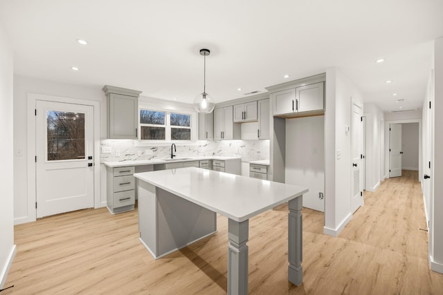 kitchen featuring a kitchen island, pendant lighting, sink, gray cabinetry, and light hardwood / wood-style flooring