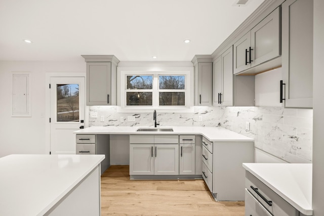 kitchen with tasteful backsplash, light hardwood / wood-style floors, gray cabinets, and sink