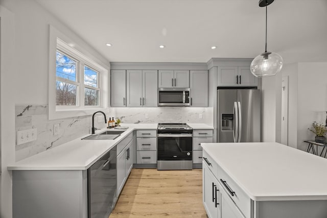 kitchen featuring tasteful backsplash, sink, gray cabinetry, hanging light fixtures, and stainless steel appliances