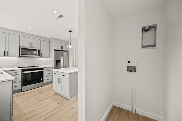 kitchen featuring stainless steel appliances, tasteful backsplash, light hardwood / wood-style flooring, and decorative light fixtures