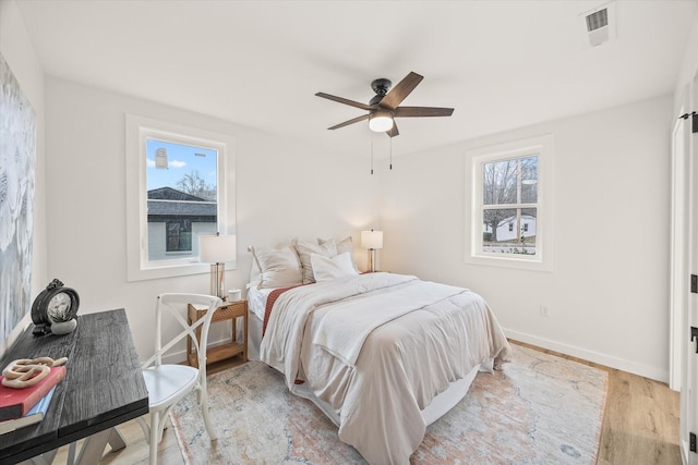 bedroom featuring ceiling fan, multiple windows, and light hardwood / wood-style flooring