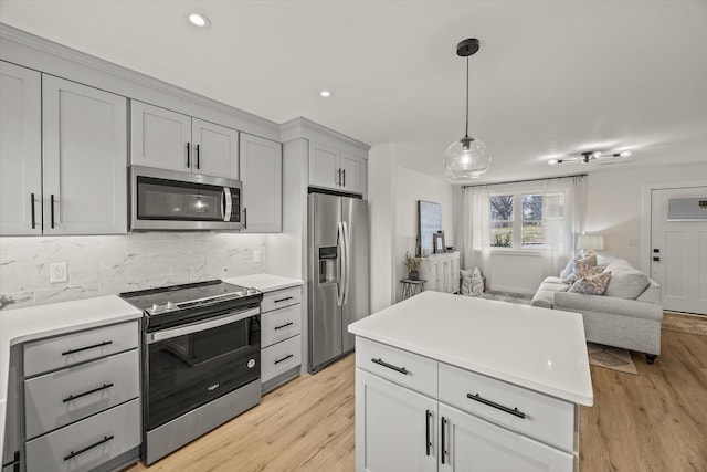 kitchen with appliances with stainless steel finishes, decorative light fixtures, tasteful backsplash, gray cabinetry, and light wood-type flooring