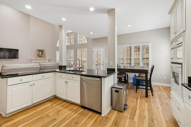 kitchen with sink, stainless steel dishwasher, white double oven, kitchen peninsula, and white cabinets