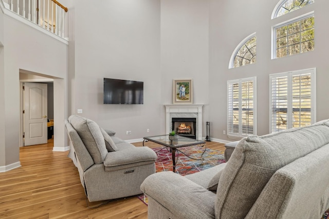 living room with a towering ceiling, a high end fireplace, and light hardwood / wood-style flooring