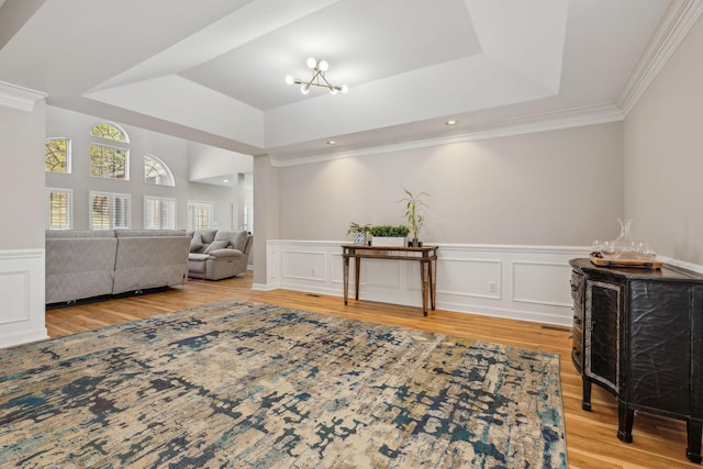 sitting room featuring a raised ceiling, wood-type flooring, ornamental molding, and a notable chandelier