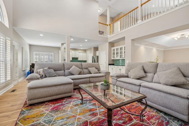 living room featuring wood-type flooring, ornamental molding, and a high ceiling