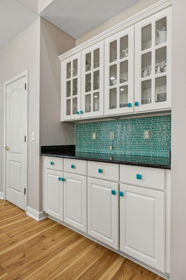 bar featuring white cabinetry, dark stone counters, light hardwood / wood-style flooring, and backsplash