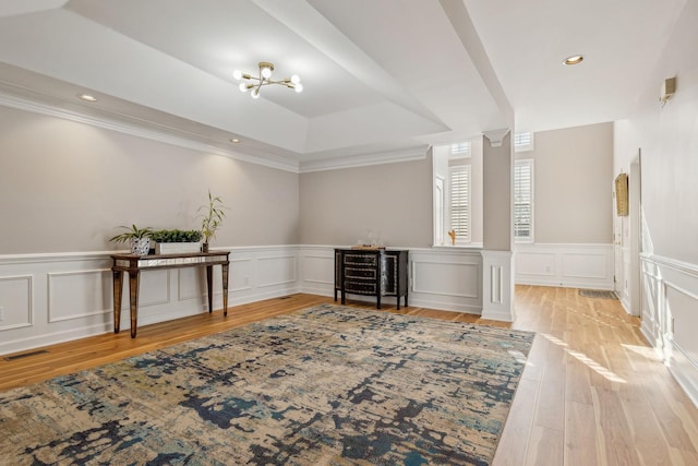 interior space with decorative columns, ornamental molding, a tray ceiling, an inviting chandelier, and light hardwood / wood-style flooring