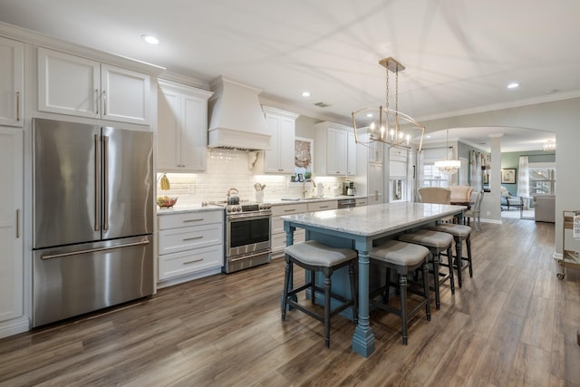 kitchen with white cabinetry, appliances with stainless steel finishes, a kitchen island, custom range hood, and light stone countertops