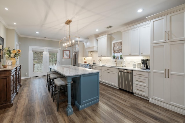 kitchen featuring stainless steel appliances, custom range hood, white cabinets, and a center island