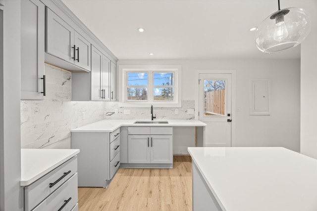 kitchen featuring pendant lighting, sink, gray cabinetry, decorative backsplash, and light hardwood / wood-style flooring