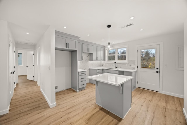 kitchen with hanging light fixtures, gray cabinets, a kitchen island, light hardwood / wood-style floors, and backsplash