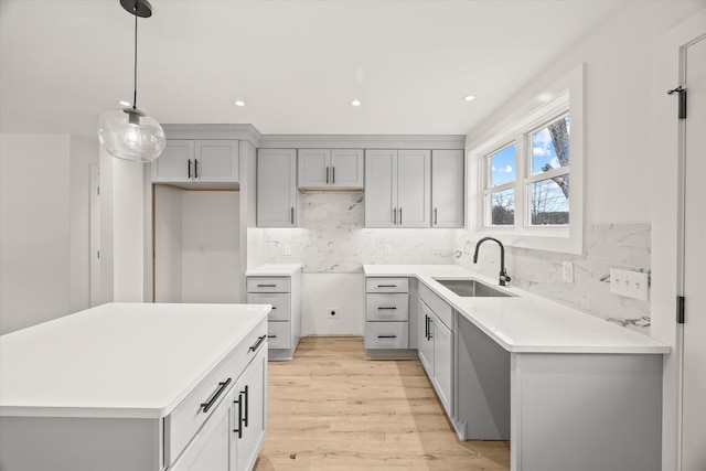 kitchen featuring decorative light fixtures, tasteful backsplash, sink, a center island, and light hardwood / wood-style floors