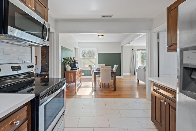 kitchen featuring stainless steel appliances, ornamental molding, a healthy amount of sunlight, and decorative backsplash