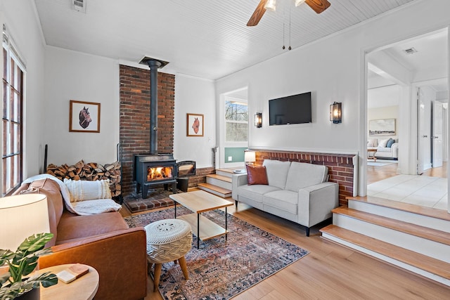 living room featuring ceiling fan, a wood stove, and light hardwood / wood-style floors