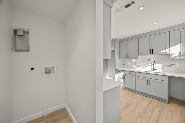 interior space with tasteful backsplash, light hardwood / wood-style floors, sink, and gray cabinetry