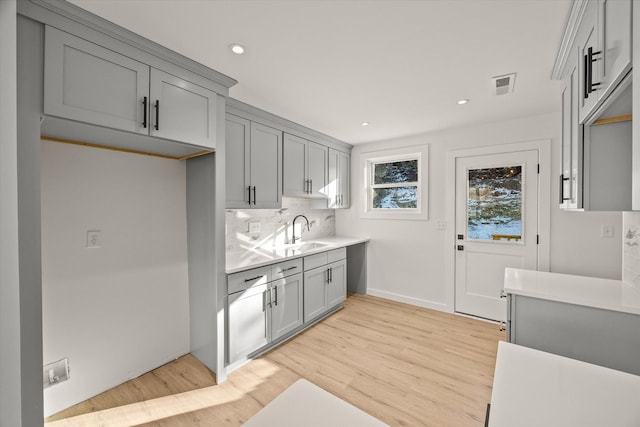 kitchen with gray cabinets, backsplash, and light wood-type flooring