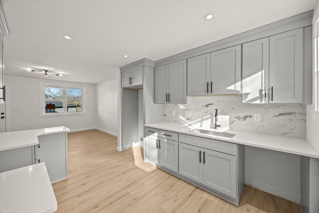 kitchen with gray cabinets, tasteful backsplash, sink, and light wood-type flooring