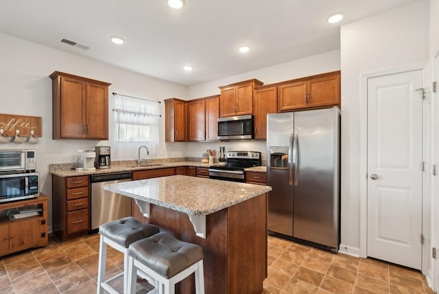 kitchen with appliances with stainless steel finishes, sink, a breakfast bar area, a center island, and light stone counters