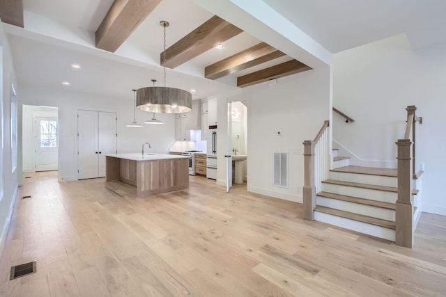 kitchen featuring high end white refrigerator, decorative light fixtures, light wood-type flooring, stainless steel range with gas cooktop, and a kitchen island with sink