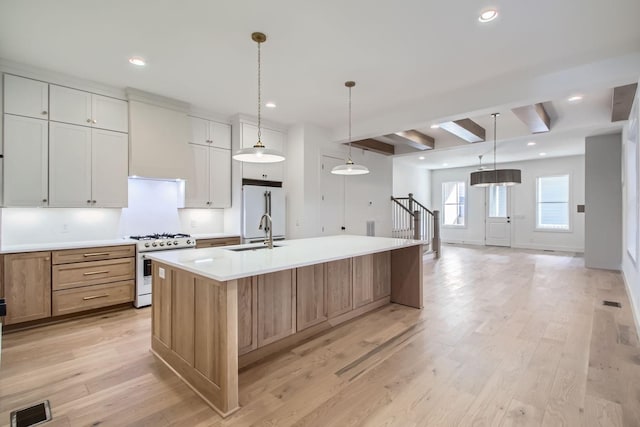 kitchen featuring sink, a large island with sink, pendant lighting, white appliances, and white cabinets