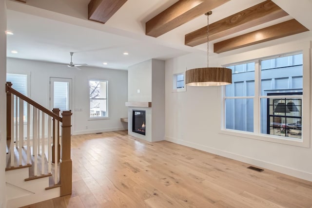 unfurnished living room featuring beamed ceiling, ceiling fan, and light wood-type flooring