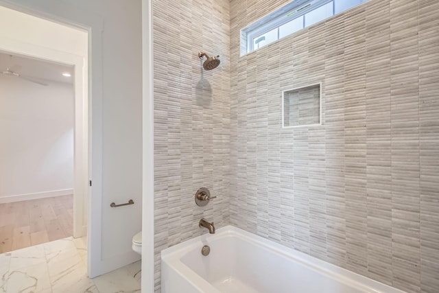 bathroom featuring tiled shower / bath combo and toilet