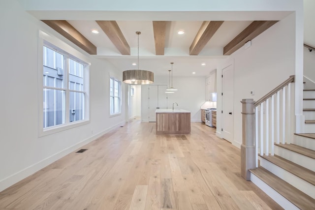 kitchen featuring hanging light fixtures, light hardwood / wood-style flooring, stainless steel stove, an island with sink, and beam ceiling