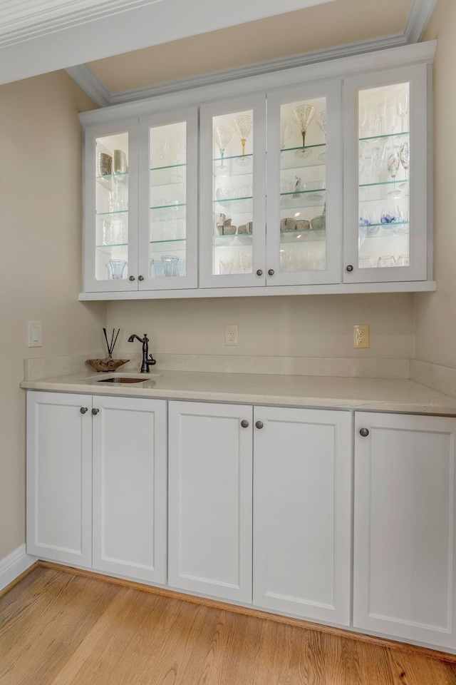 bar featuring sink, crown molding, light hardwood / wood-style floors, and white cabinets