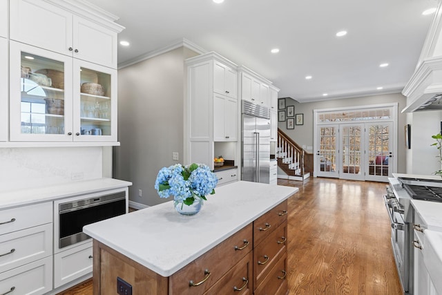 kitchen with white cabinetry, built in appliances, ornamental molding, a kitchen island, and hardwood / wood-style floors