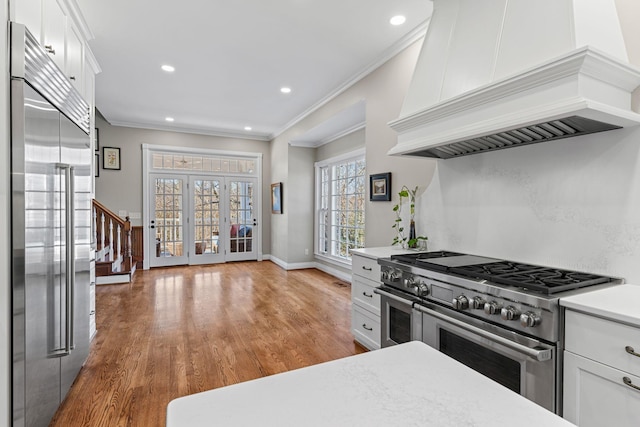 kitchen featuring crown molding, white cabinetry, high end appliances, light hardwood / wood-style floors, and custom exhaust hood