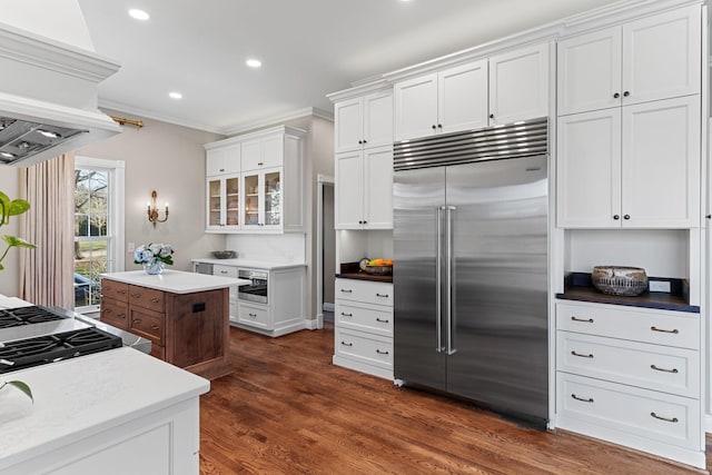 kitchen featuring ventilation hood, white cabinetry, stainless steel built in refrigerator, crown molding, and dark wood-type flooring