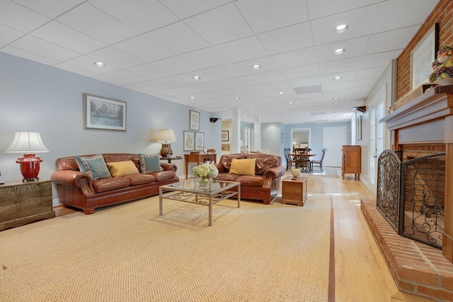 living room with a brick fireplace, light hardwood / wood-style flooring, and a drop ceiling