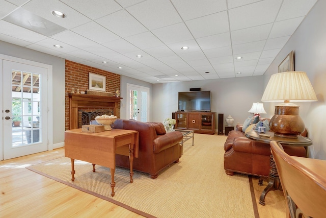 living room with a paneled ceiling, wood-type flooring, and a brick fireplace