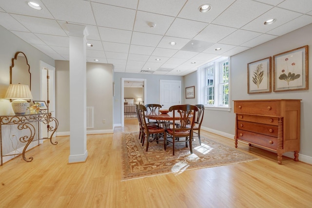 dining area featuring ornate columns, a drop ceiling, and light wood-type flooring