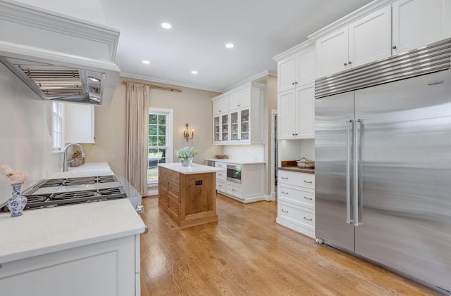 kitchen featuring crown molding, light hardwood / wood-style flooring, stainless steel built in refrigerator, white cabinets, and a kitchen island