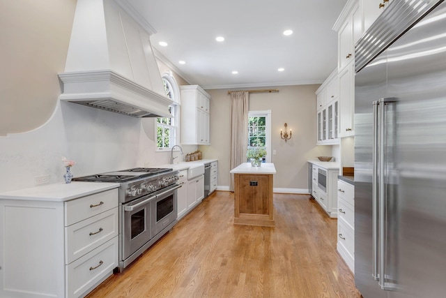 kitchen featuring a kitchen island, white cabinets, custom exhaust hood, built in appliances, and light wood-type flooring