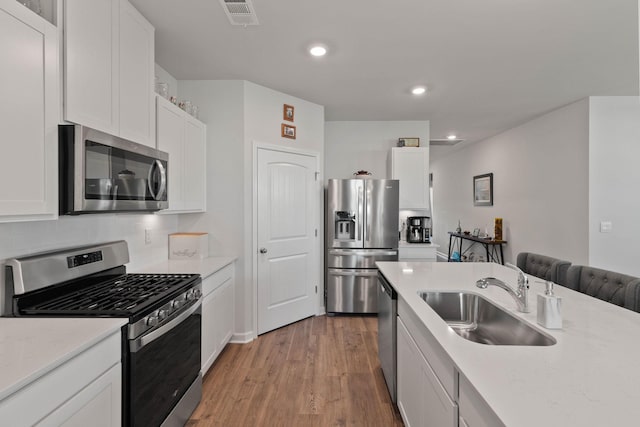 kitchen with sink, white cabinetry, stainless steel appliances, tasteful backsplash, and light wood-type flooring