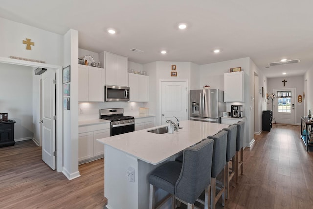 kitchen with stainless steel appliances, sink, a kitchen island with sink, and white cabinets