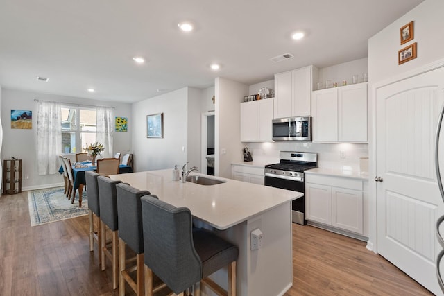 kitchen with white cabinetry, stainless steel appliances, a kitchen island with sink, and sink