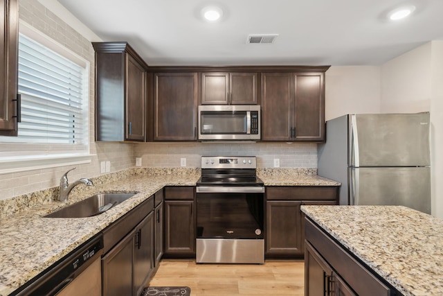 kitchen featuring sink, appliances with stainless steel finishes, light stone counters, tasteful backsplash, and light hardwood / wood-style floors