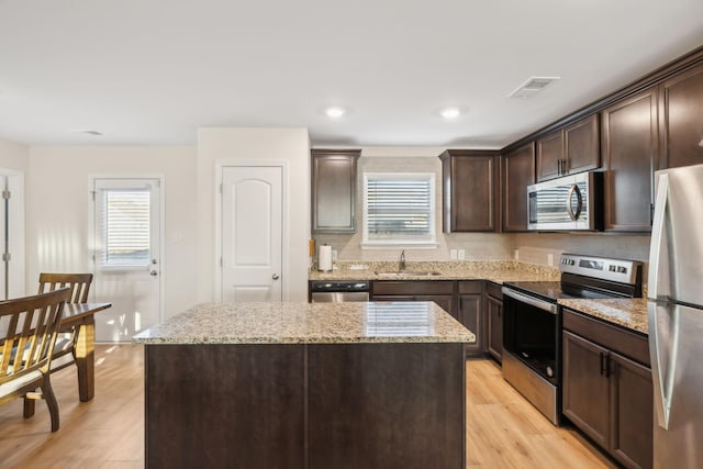 kitchen with a kitchen island, light stone countertops, appliances with stainless steel finishes, and sink