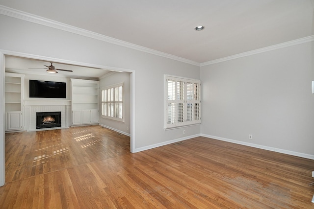 unfurnished living room with a fireplace, wood-type flooring, ceiling fan, crown molding, and built in shelves