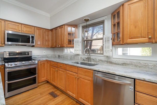 kitchen with sink, hanging light fixtures, ornamental molding, stainless steel appliances, and light stone countertops