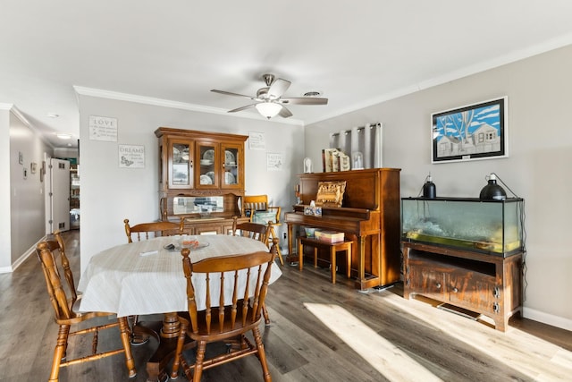 dining room with dark wood-type flooring, ornamental molding, and ceiling fan