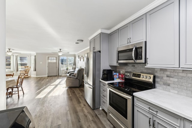 kitchen featuring crown molding, appliances with stainless steel finishes, gray cabinetry, dark hardwood / wood-style floors, and decorative backsplash