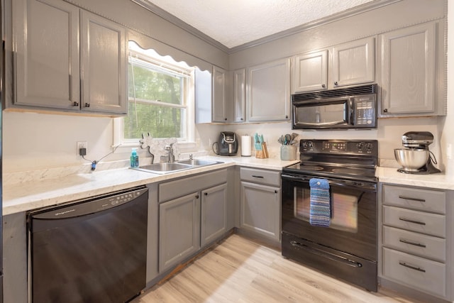 kitchen with sink, crown molding, gray cabinets, black appliances, and light wood-type flooring