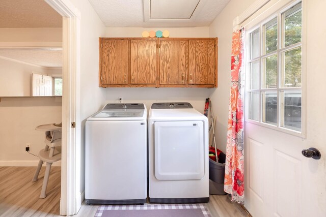 clothes washing area with cabinets, washing machine and dryer, light hardwood / wood-style flooring, and a textured ceiling