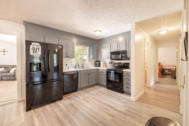 kitchen with gray cabinetry, a textured ceiling, light hardwood / wood-style flooring, and black appliances